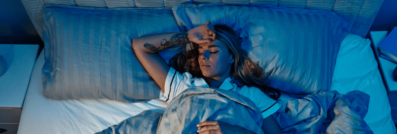 Woman lying awake in bed at night with hand on forehead showing difficulty with sleep after surgery.